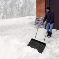 Mężczyzna odśnieżający podjazd dużym pługiem w kolorze czarnym, który można kupić w naszym sklepie